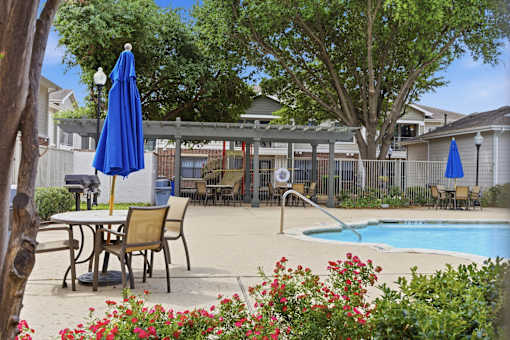 A pool area with a table and chairs and umbrellas.