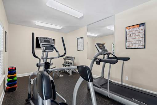 A gym with a treadmill, elliptical trainer and a mirror.