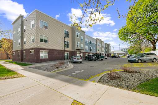 A row of apartment buildings with cars parked in front.