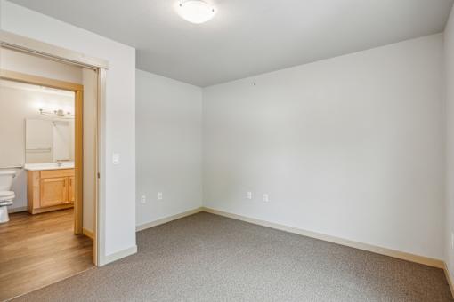 A white room with a carpeted floor and a doorway leading to a bathroom.