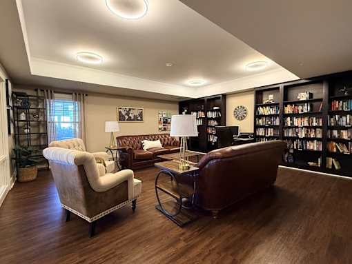 A living room with a brown leather couch, a white armchair, and a coffee table.at The Lodge at Johns Road Apartments, Huntsville, AL, 35806