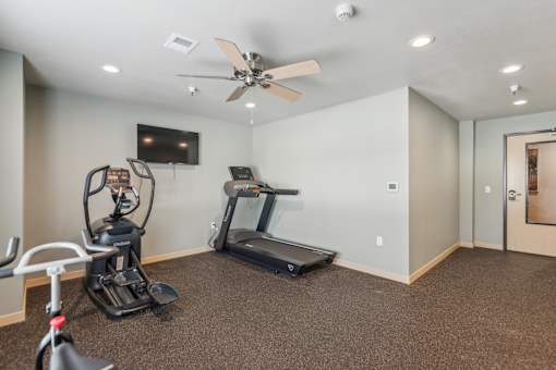 A spacious room with a treadmill, exercise bike, and television.