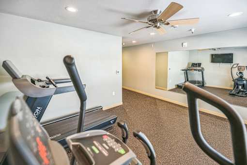 A treadmill in a room with a ceiling fan and exercise equipment.