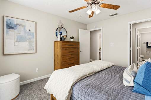 A bedroom with a bed, dresser, and a ceiling fan.