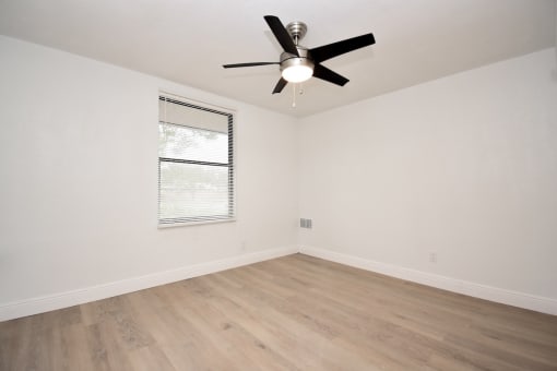 an empty living room with a ceiling fan and a window