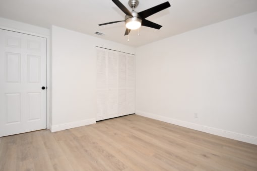 an empty living room with a ceiling fan and a closet