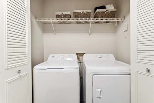 A laundry room with two washing machines and a shelf above them.