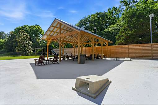 A pavilion with a roof made of wooden beams is surrounded by a concrete floor and a wooden fence.