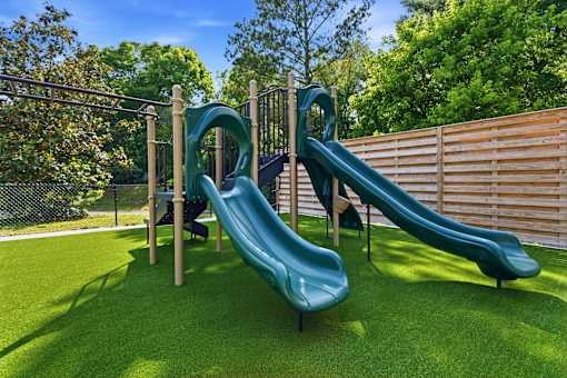 A playground with a green slide and a wooden fence.