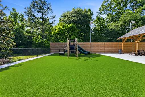 A green artificial turf in a backyard with a slide and wooden fence.