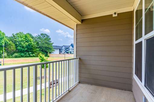 A balcony with a metal railing and a view of a green lawn and trees.