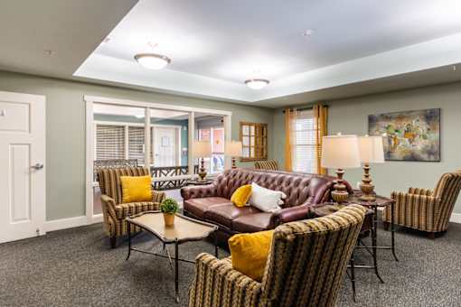 A living room with a brown leather couch and striped chairs.