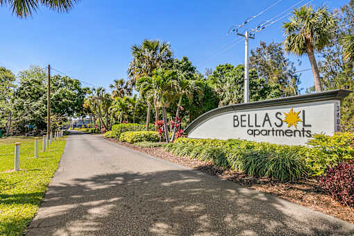 A street view of Bellas Apartments with a sign and a road.