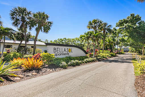 A road leading to a sign that says Bellas Apartments.