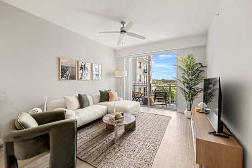 A living room with a white couch, a coffee table, a flat screen TV, and a sliding glass door leading to a balcony.