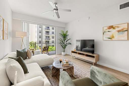 A living room with a white couch, a green chair, a wooden coffee table, a flat screen TV, and a ceiling fan.