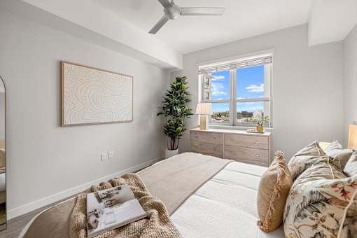 A bedroom with a large bed, a ceiling fan, and a window with a view of the city.