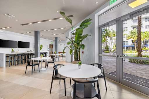 A white table with chairs is in the foreground of a room with a glass door leading to a patio.