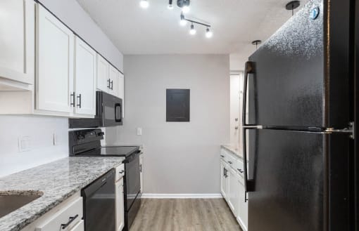 a renovated kitchen with white cabinets, quartz countertops, and black appliances