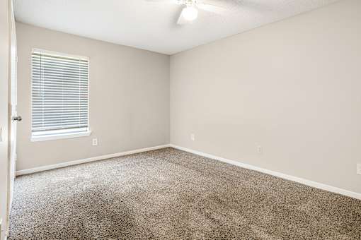 A room with a carpeted floor and a window with blinds.