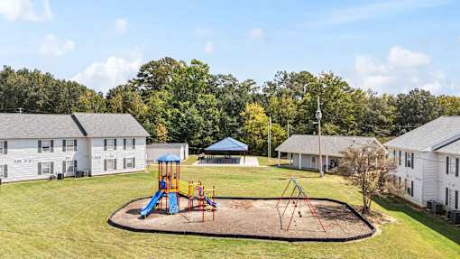 A playground with a blue slide and red swings in the middle of a grassy area.