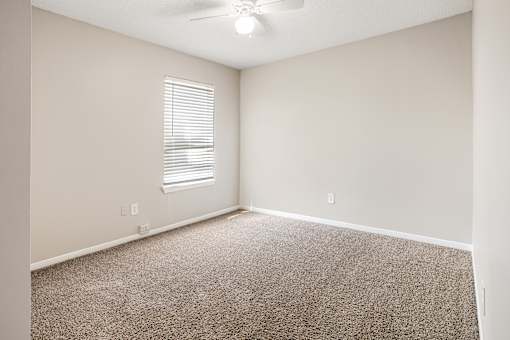 A room with a carpeted floor and a window with blinds.