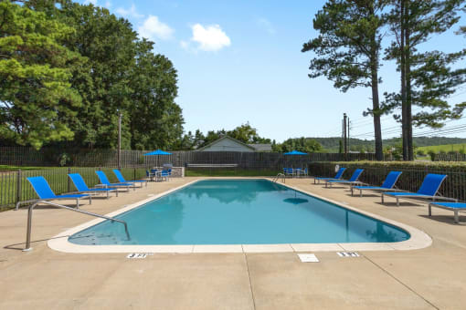 a swimming pool with blue chairs around it and trees