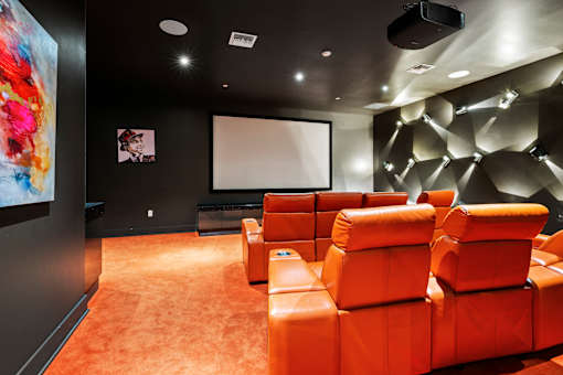A room with orange seats and a large screen on the wall.