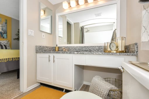 Model apartment bathroom with granite countertops, a large mirror, and ample lighting at The Oasis Daytona