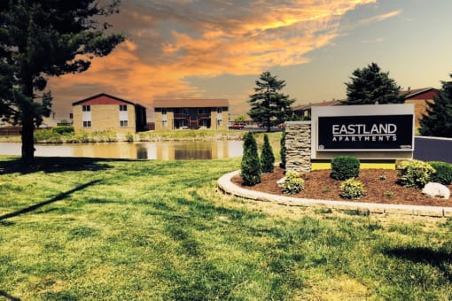 The monument sign in front of Eastland Apartments lush grounds, pond, and residential buildings