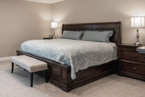 a bedroom plush pillows on a bed and two night stands with lamps and a bench