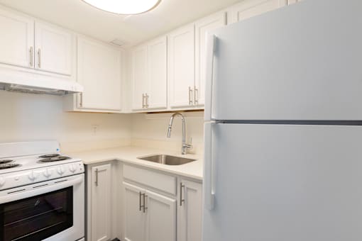 A white kitchen with a refrigerator, oven, and sink.