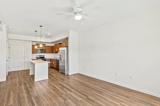 an empty living room with a kitchen and a ceiling fan