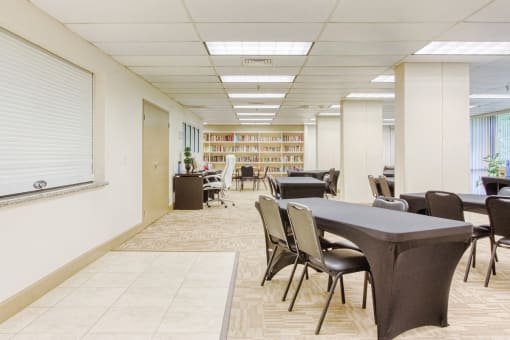 large community room with tables and chairs by computer station & library