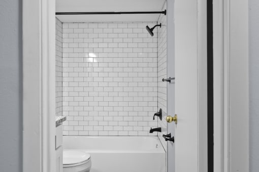 a bathroom with white subway tile and a tub and a toilet