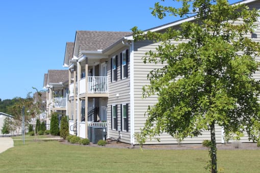 Apartment homes with balconies, trim grass, trees, and AC units