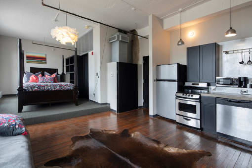 Furnished model with bed on platform, stainless steel in kitchen, and hardwood floors at Jemison Flats, Birmingham