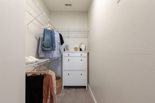 a walk in closet with clothes hanging on the wall and a dresser in it