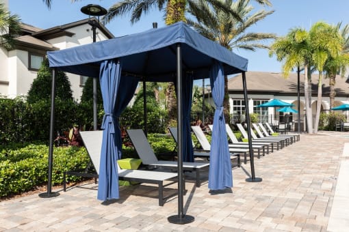 a row of lounge chairs under a blue gazebo with umbrellas