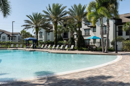 a large swimming pool with palm trees in front of an apartment building