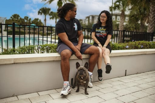 two people sitting on low wall by pool with dog on a leash