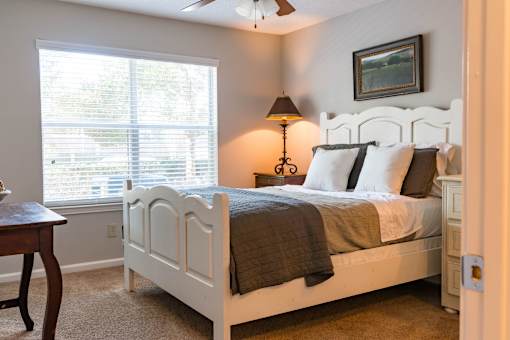 A bedroom with a white bed and a window with blinds.