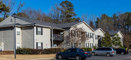 A grey and white two story apartment building with a parking lot in front.