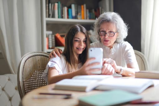a young girl and older woman sitting at a table together looking at a cell phone