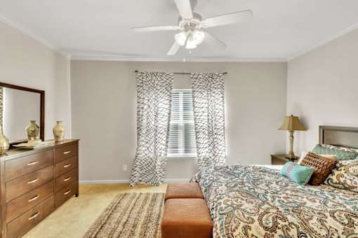 A bedroom with a bed, dresser, and window with curtains.