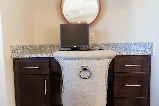 A black computer monitor sits on a desk with a round mirror above it.