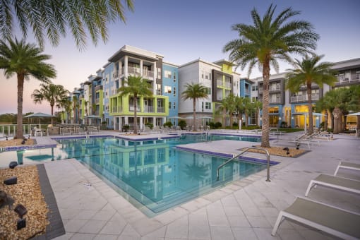 The swimming pool and large pool deck with towering palms and apartment homes at Residences at The Green in Lakewood Ranch