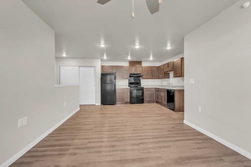 an empty living room with a kitchen with black appliances