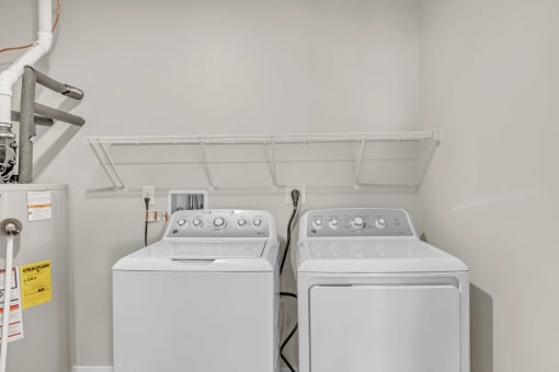 two washes and a dryer in a laundry room with a shelf above them