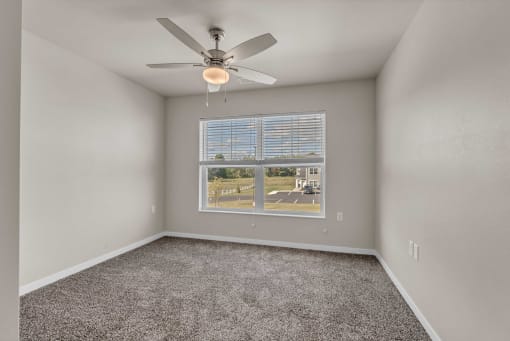 an empty room with a large window and a ceiling fan